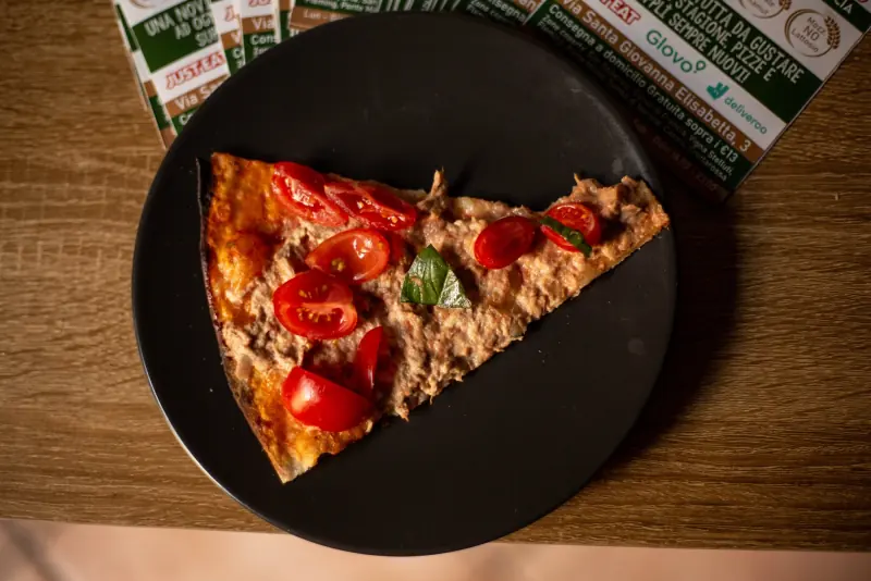 Uno spicchio di pizza rossa con pomodorini su un piatto nero