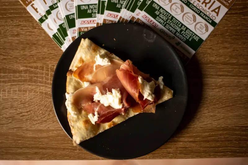 Uno spicchio di pizza con prosciutto crudo e stracciatella
